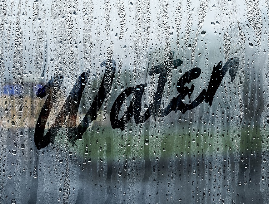 Close up of a window covered in raindrops with the word 'water' written in the condensation.