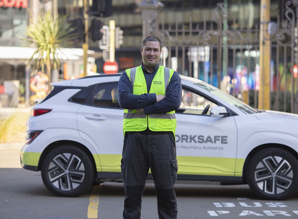 man in a high vis vest stands in front of a WorkSafe car with his arms crossed