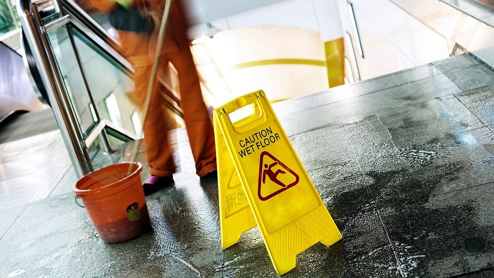 worker mops near a sign with text that reads caution wet floor