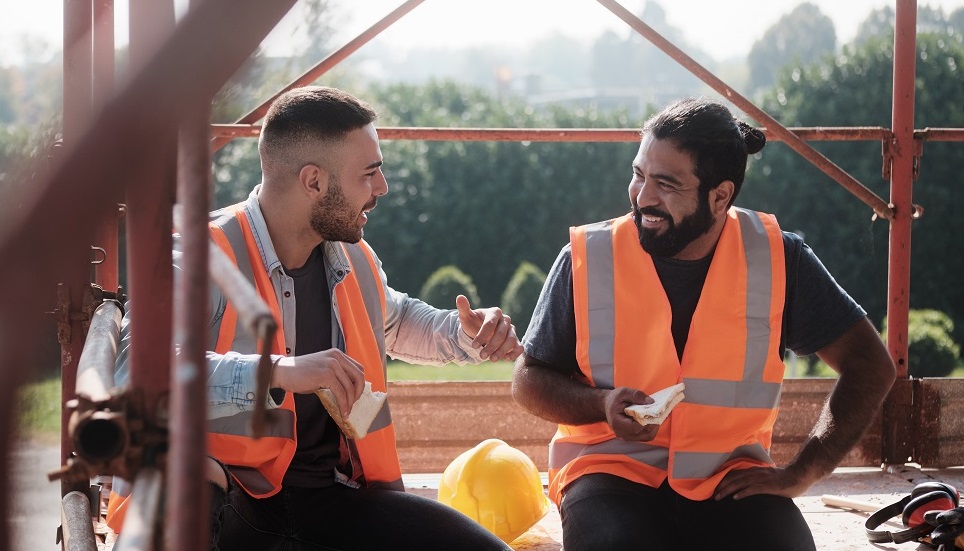 two workers talking and eating sandwiches