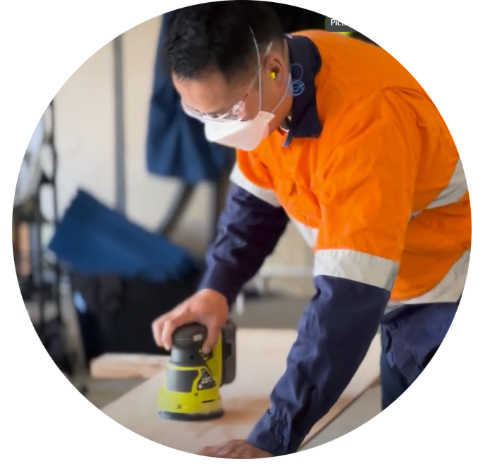 Photo cropped into a circle of a person sanding while wearing a dust mask