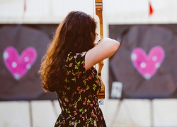 A photo of someone aiming a bow and arrow at a heart-shaped target